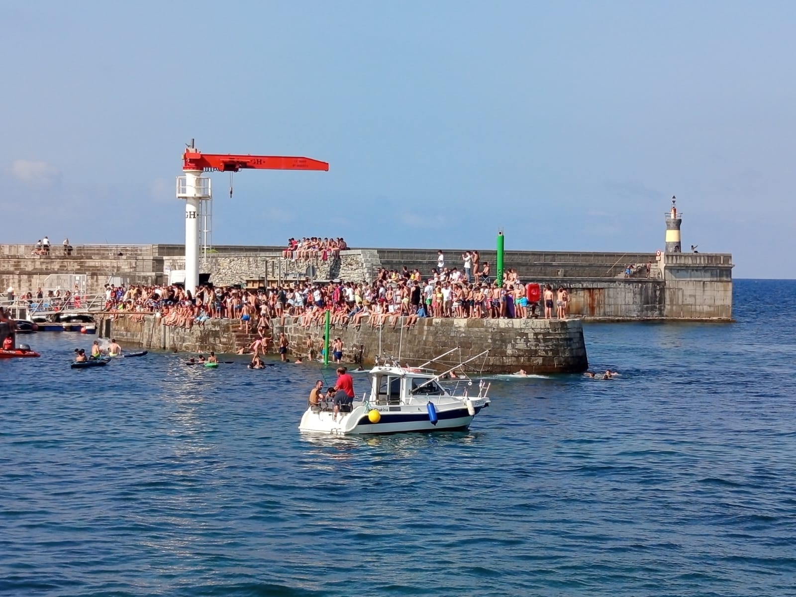 Crowd on a pier with boats nearby, clear blue sky and sea.