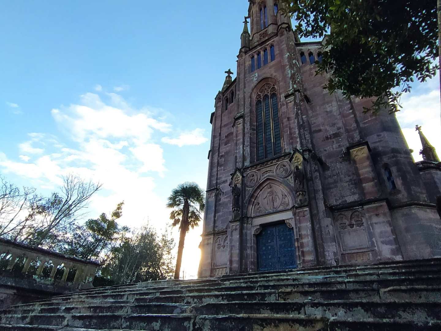 Gothic-style church with tall spire under a blue sky, viewed from stone steps below.
