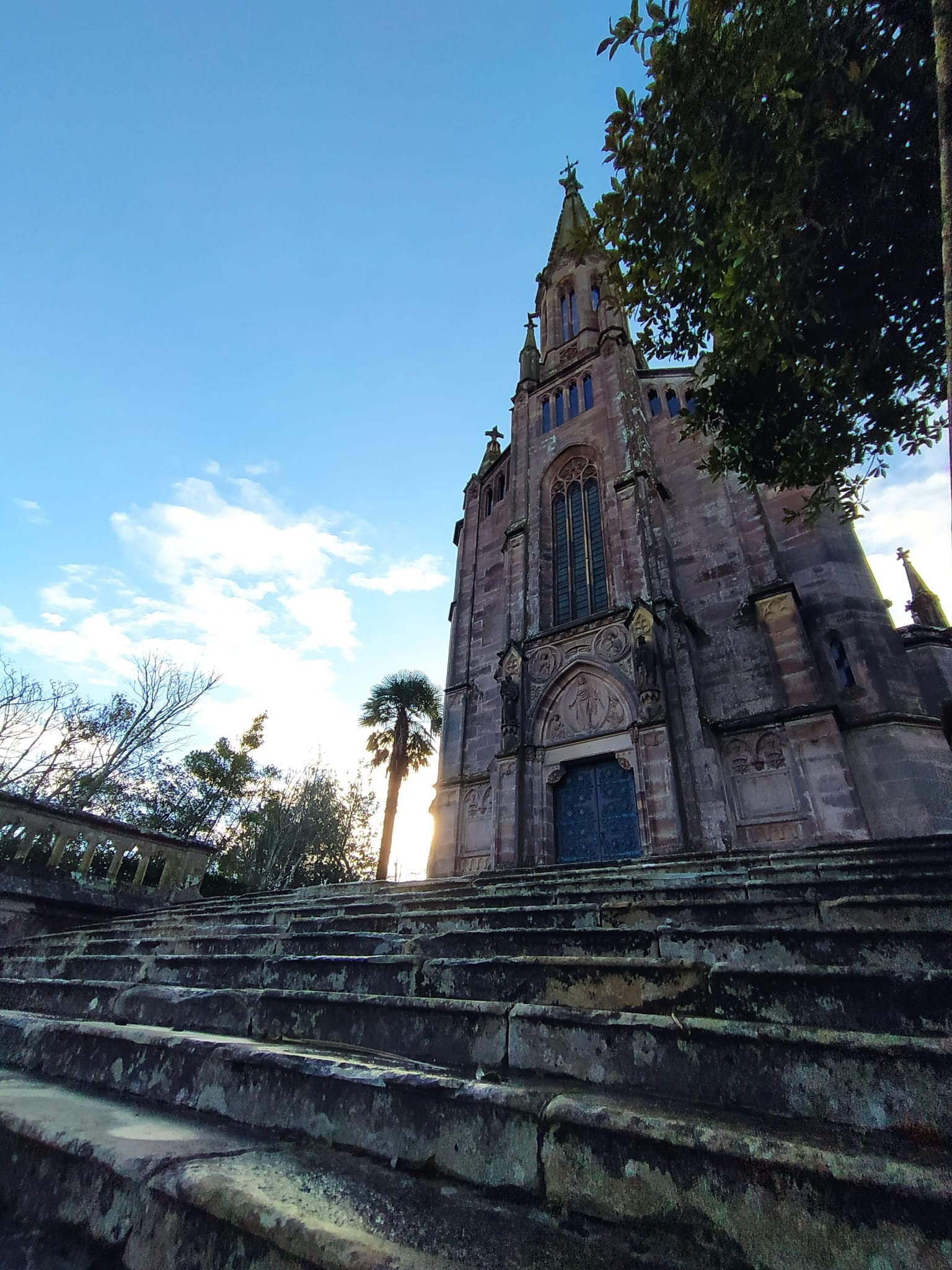 Gothic-style church with tall spire under a blue sky, viewed from stone steps below.