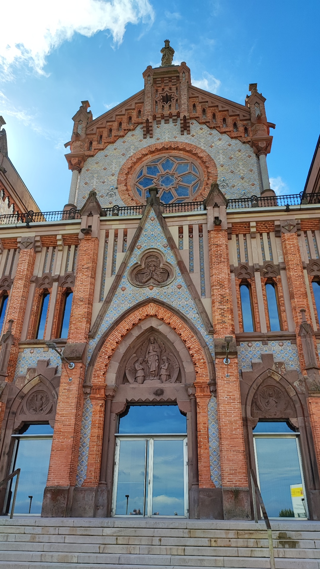 Front view of a brick Gothic-style church facade against a blue sky.