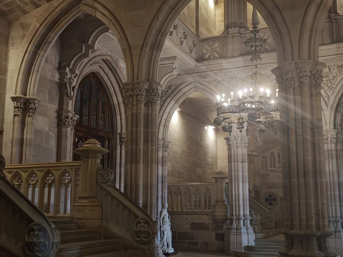 Grand stone staircase with arches and ornate chandeliers in a historic building.