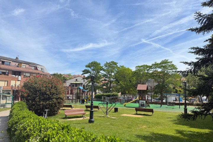Park with playground, benches, and trees under a blue sky.