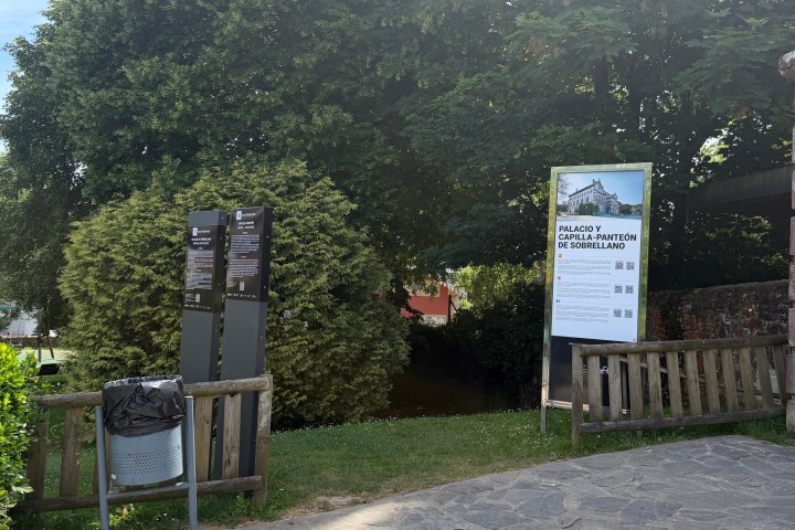 Park entrance with signs and lush greenery under a sunny sky.