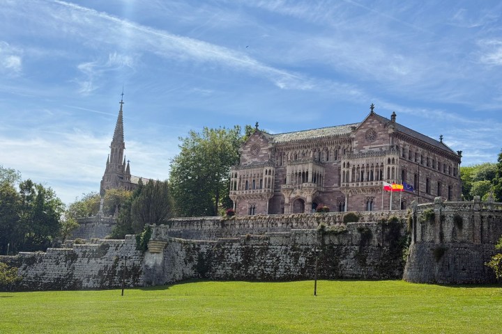 Historic building with ornate architecture and a large lawn, under a blue sky.